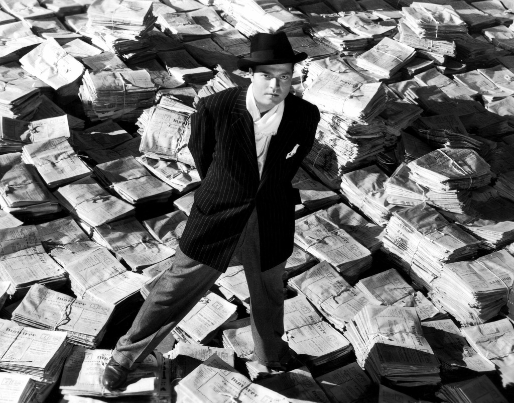 Citizen Kane standing amidst stacks of newspapers
